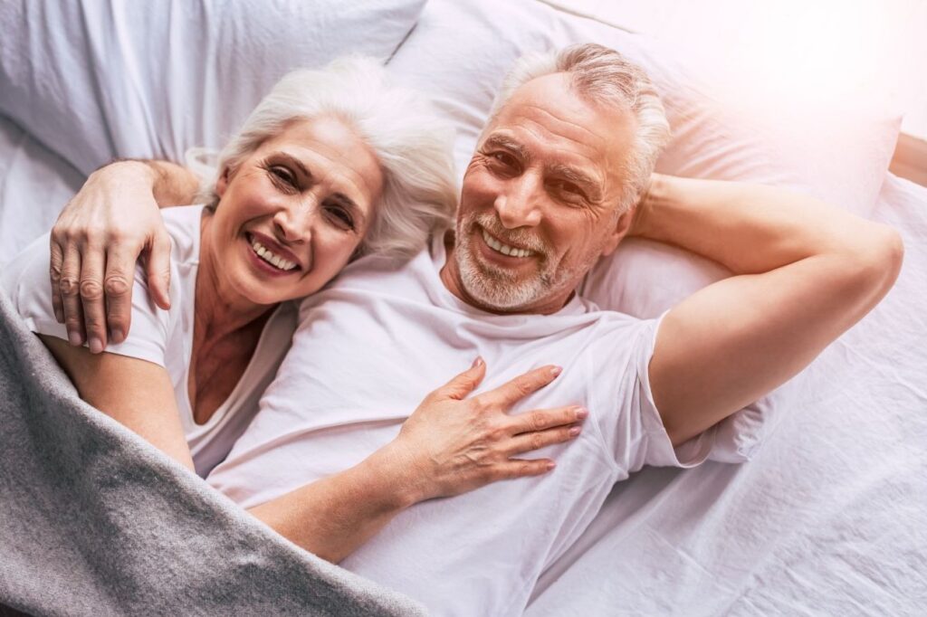 Older white couple in bed smiling.